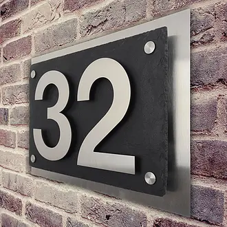 Moderne Edelstahl Hausnummer mit Schiefer an rustikaler Backsteinwand
