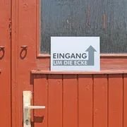 Schild Eingang um die Ecke
